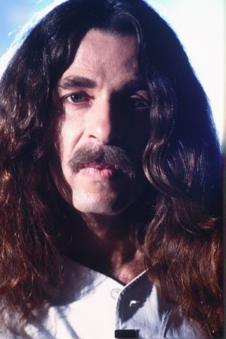 Man with long hair and a mustache gazes directly at the camera.
