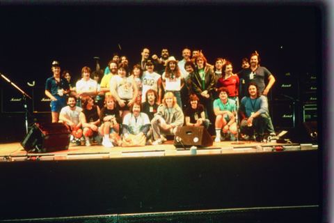 Group of people posing together on stage in front of amplifiers.